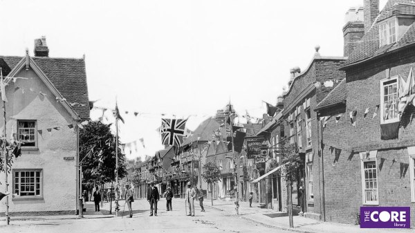 Black and white photograph showing the top end of Solihull High Street, with flags and bunting across the street. A small crowd of adults stand looking at the photographer.